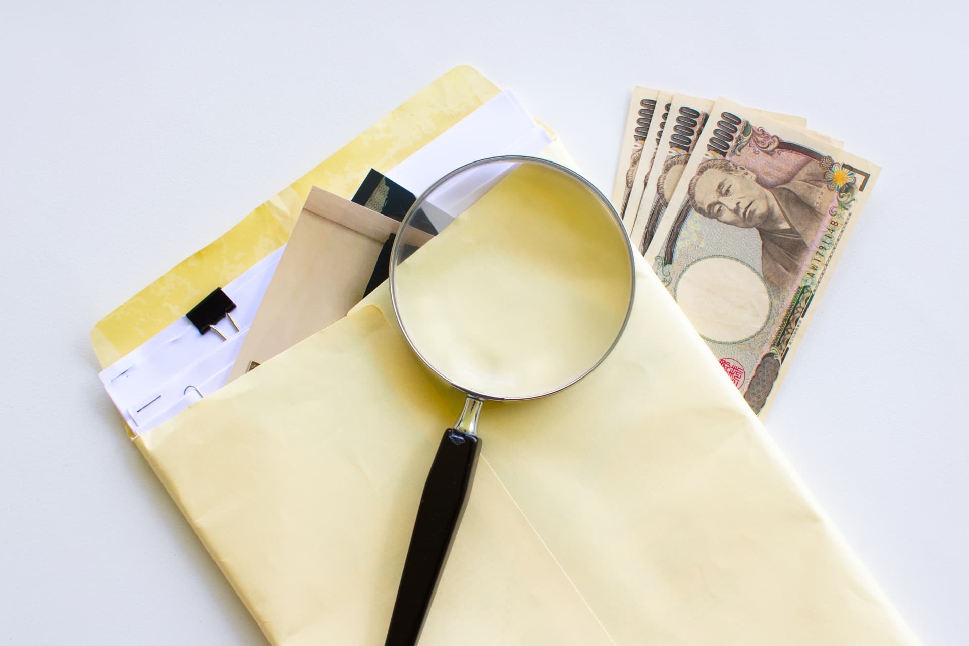 調査書類と虫眼鏡とお金の画像